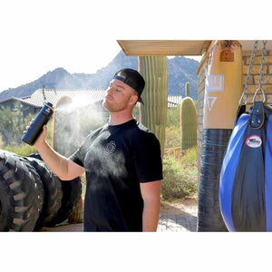 Man using an ExtremeMIST water bottle to spray a cooling mist on his face outdoors