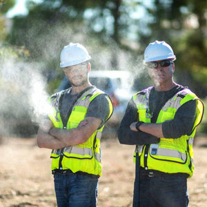 Two construction workers in hard hats and high visibility vests standing outdoors with mist in the air