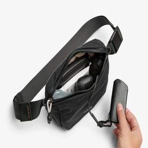 Bellroy black sling bag with open main compartment containing personal items and a hand holding a key cover