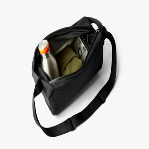Open black Bellroy sling bag containing a metal water bottle, camera, and folded green fabric