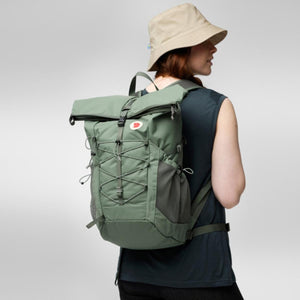 Person wearing a green Fjallraven rolltop backpack with bungee cord detail