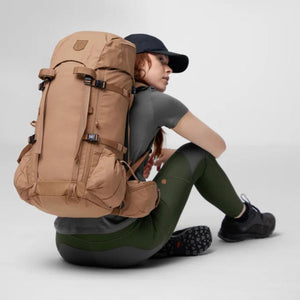 Person wearing a tan Fjallraven hiking backpack while sitting on the floor