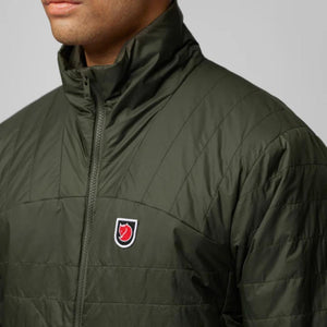 Person wearing a dark green FjallRaven quilted jacket with a high collar and brand logo patch