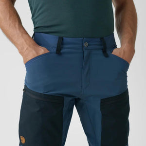 Fjallraven blue trekking trousers with black thigh pockets and hands in pockets