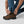 Person adjusting the snap button on the hem of blue hiking trousers over brown leather hiking boots