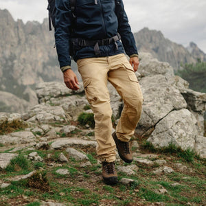 Person hiking in FjallRaven beige cargo trousers and dark jacket on a rocky mountain trail