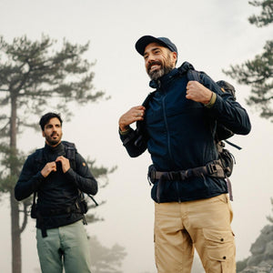 Two men wearing FjallRaven hiking gear and backpacks standing in a forest