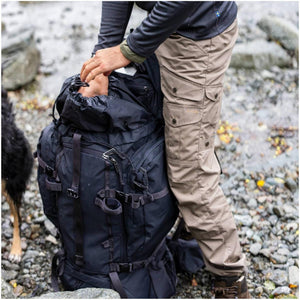 Person wearing FjallRaven trousers opening a black hiking backpack outdoors
