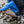 Person wearing Fjallraven blue jacket and beige trousers crouching on rocky stream bank with black backpack