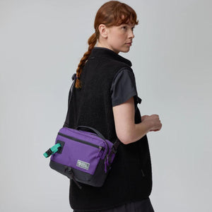 Person wearing a purple Fjallraven crossbody bag over a black fleece vest