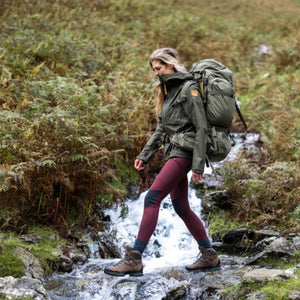 Hiker wearing FjallRaven jacket and backpack crossing a stream