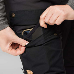 Hand placing a smartphone into the side pocket of black FjallRaven trousers
