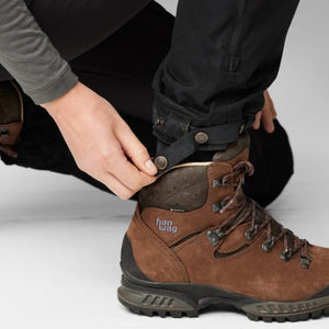 Person adjusting the snap button strap on the hem of black FjallRaven trousers over a brown Hanwag hiking boot