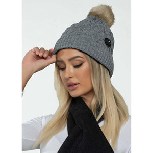 Woman wearing a grey cable knit beanie with a pom pom and integrated Bluetooth speaker