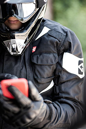 Motorcyclist wearing black Acerbis jacket and helmet holding a red smartphone