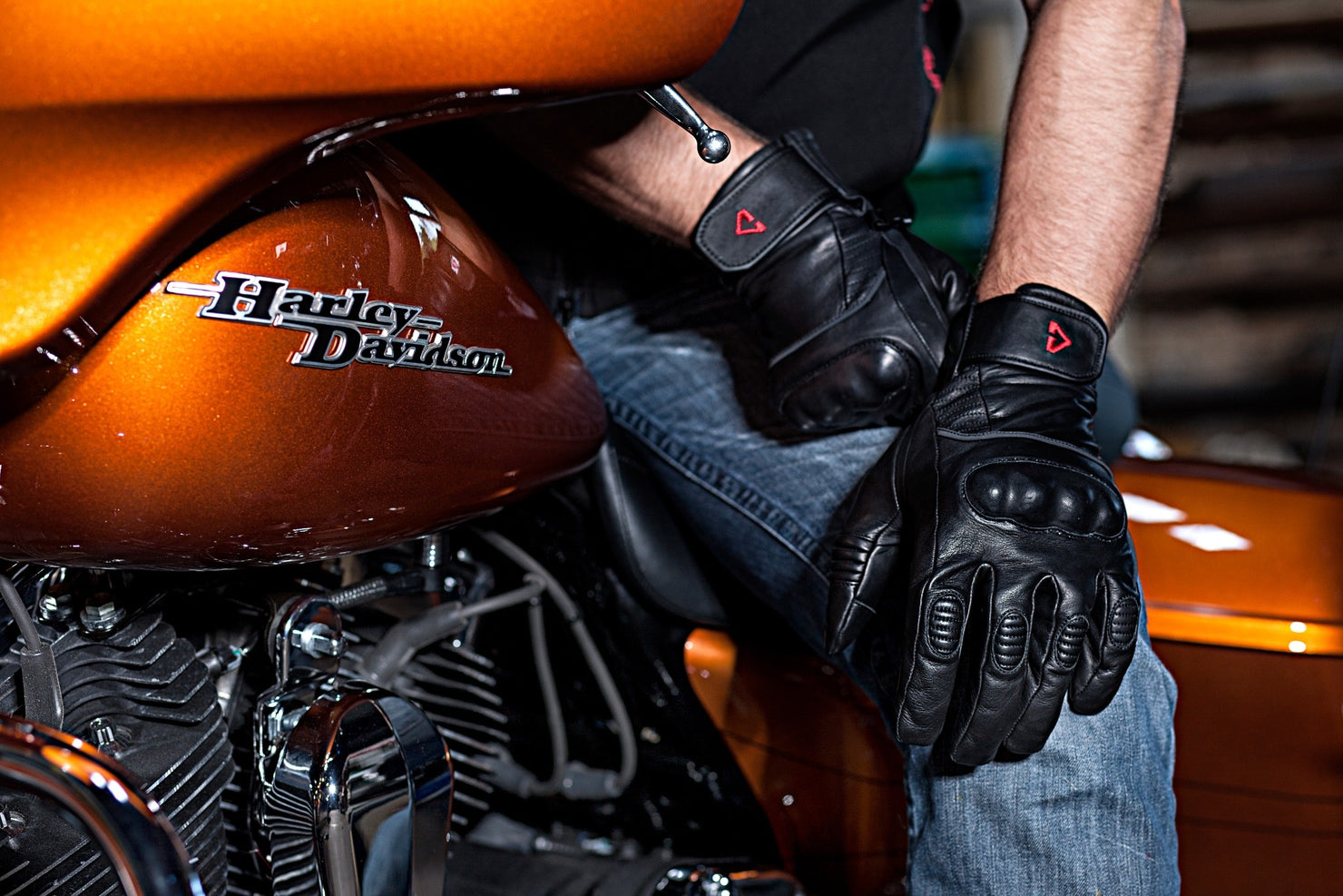 Person wearing black leather motorcycle gloves sitting on a Harley Davidson motorcycle