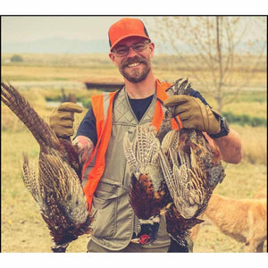 Man wearing Glacier Glove hunting gloves holding three pheasants in a field