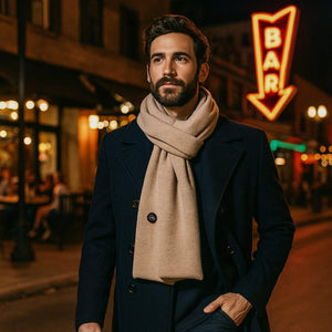Man wearing a Gobi Heat beige scarf and dark coat on a city street at night