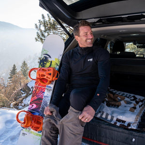 Man wearing Gobi Heat black base layer sitting in vehicle trunk with snowboard