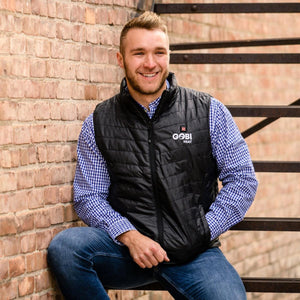 Man wearing a black Gobi Heat quilted vest over a blue gingham shirt