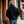 Person seen from behind wearing a black hooded sweatshirt and blue jeans walking on a sidewalk