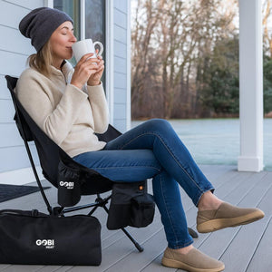Woman sitting in a Gobi Heat camping chair on a deck drinking from a white mug