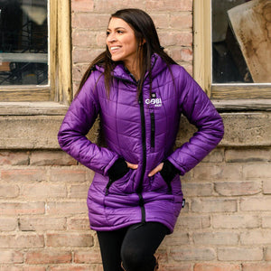 Woman wearing a purple Gobi Heat hooded puffer jacket against a brick wall