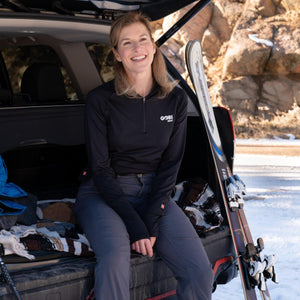 Woman wearing a black Gobi Heat long sleeve shirt sitting in the back of a car with skis