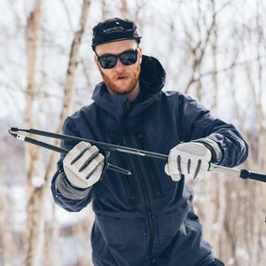 Person wearing Gordini gloves assembling a folding ski pole in a snowy forest