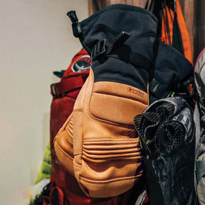 Gordini tan leather and black fabric winter mitten hanging in front of backpacks