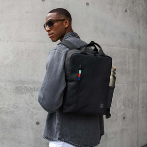 Person wearing a black Got Bag backpack with a water bottle in the side pocket against a concrete wall