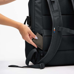 Hand placing a brown wallet into the side pocket of a black Got Bag backpack