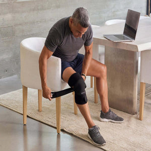 Person sitting at a table adjusting a black Gravity knee brace