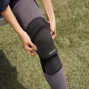 Person adjusting a black Gravity knee brace over leggings