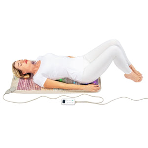 Person lying on a HealthyLine rainbow gemstone mat with a digital controller