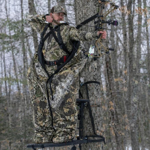 Hunter in camouflage insulated suit aiming a compound bow from a tree stand