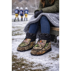 Person wearing Heater Body Suit camouflage insulated boots while sitting on a bench in the snow