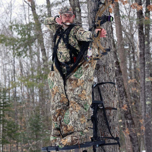 Hunter wearing camouflage insulated suit in a tree stand aiming a compound bow