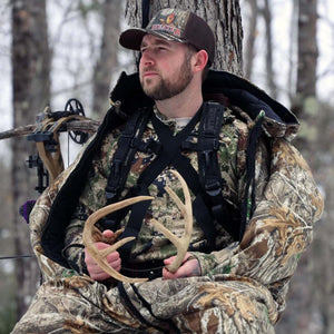 Hunter wearing Heater Body Suit camouflage gear holding deer antlers in a tree stand