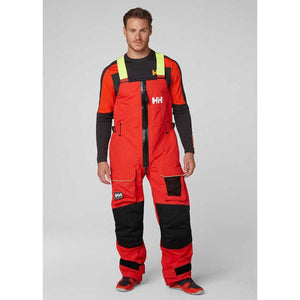 Man wearing Helly Hansen red and black sailing salopettes with high visibility yellow shoulder straps