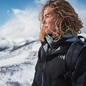 Woman with curly hair wearing a Helly Hansen jacket in a snowy mountain landscape