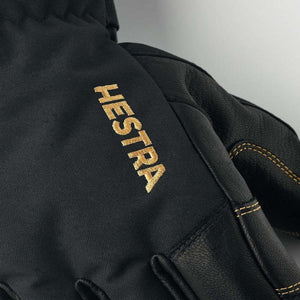 Black Hestra glove with gold embroidered logo and contrast stitching