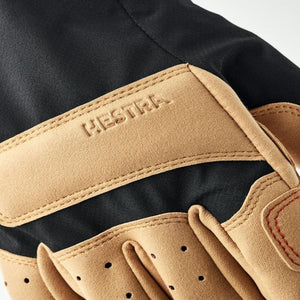 Hestra glove detail showing tan suede palm and black fabric back with embossed brand logo