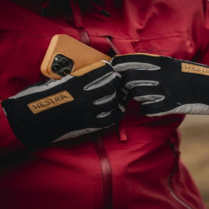 Person wearing Hestra gloves pulling a smartphone from a red jacket pocket