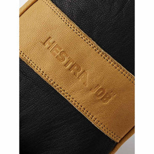 Hestra logo embossed on a tan leather strap against black textured material