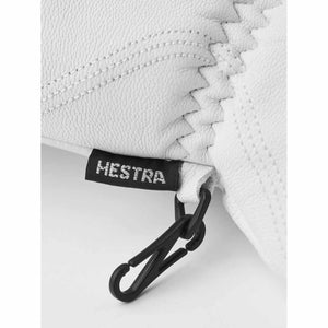 White Hestra glove detail with black brand tag and plastic carabiner clip