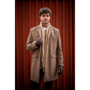 Man wearing a tan coat and Hestra brown leather gloves against a red wooden wall
