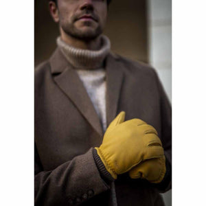 Man wearing yellow Hestra leather gloves with a brown coat and turtleneck