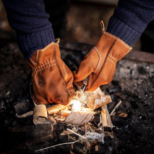 Hestra leather gloves being used to strike a fire starter against birch bark