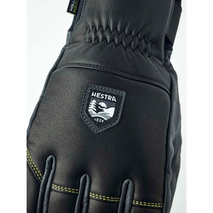 Black Hestra leather glove with yellow stitching and brand logo patch